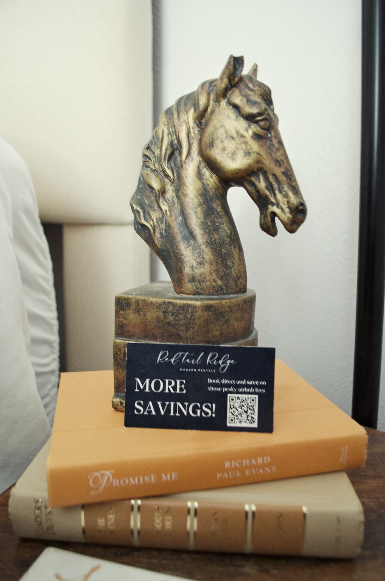 A bronze horse head sculpture on a pedestal, with a book titled 'Promise Me' by Richard Paul Evans and a promotional card for 'Rooftop Ridge' on top.