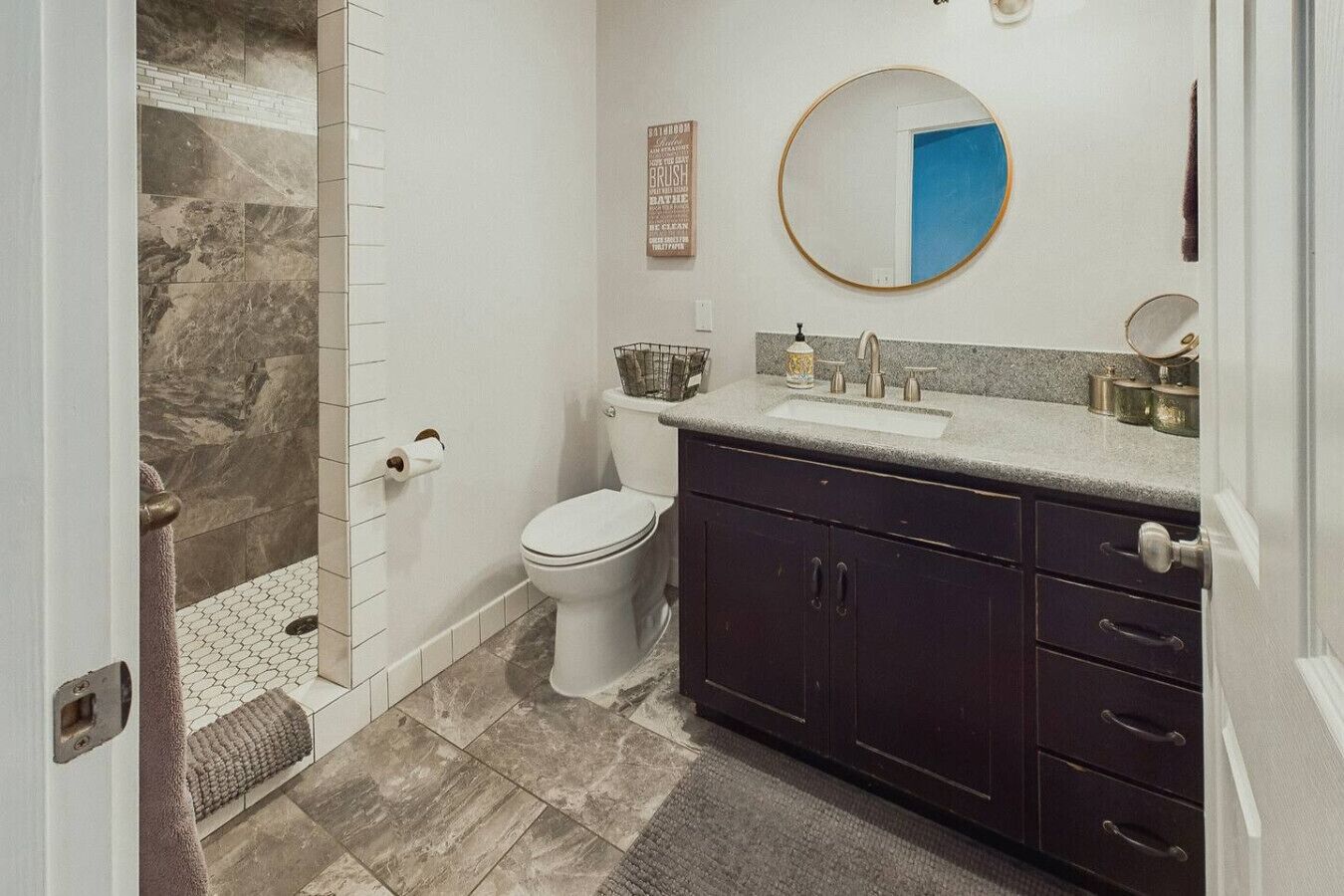 Une salle de bain comprenant des toilettes, un lavabo, des meubles sombres et un espace douche.