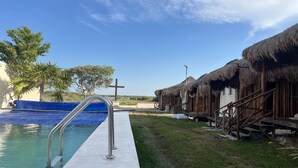 A pool area with a metal ladder, thatched-roof huts, and a clear blue sky. - Paraiso Cocoyito Ría  (Progreso)