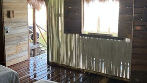 A room with a wooden floor, a bed with a white sheet, a window with a view, and a door leading outside. - Paraiso Cocoyito Ría  (Progreso)