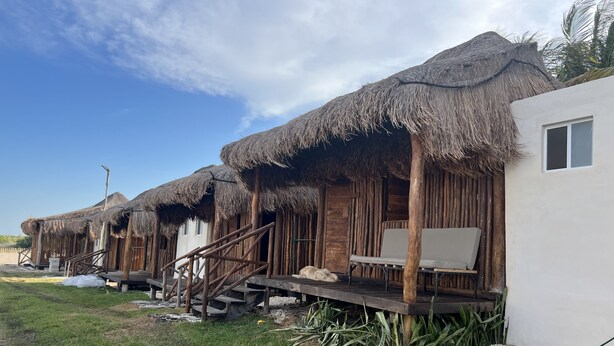 A row of thatched-roof bungalows with wooden decks and a white building adjacent to them. - Paraiso Cocoyito Ría  (Progreso)