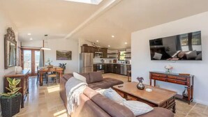A spacious living area with a brown leather sofa, a wooden coffee table, and a dining table with chairs. A kitchen is visible in the background with modern appliances. - Hilltop Villa with Panoramic Views of Carmel Valley, 30 days  (Carmel Valley)
