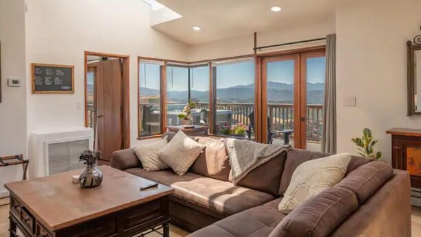 A cozy living room with a large sectional sofa, a wooden coffee table, and a view of mountains through large windows. - Hilltop Villa with Panoramic Views of Carmel Valley, 30 days  (Carmel Valley)
