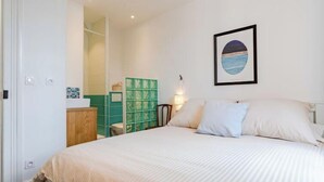 Une chambre à coucher comprenant un lit, une table de chevet, une lampe fixée au mur et un tableau représentant un paysage.