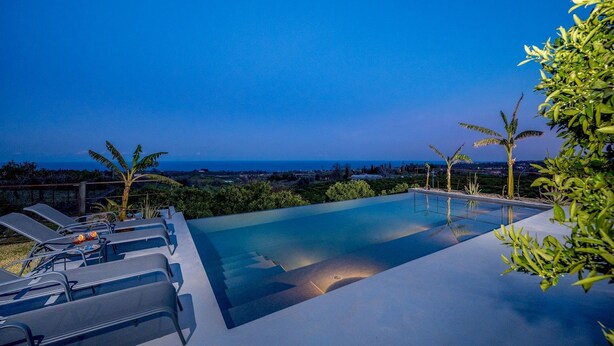 An infinity pool with lounge chairs and palm trees, overlooking a coastal landscape. - Agrume Country House 8 Emma Villas (Santa Venerina)