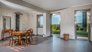 A dining area with a wooden table and chairs, a patterned rug, and a view of a garden through large sliding glass doors. - Agrume Country House 8 Emma Villas (Santa Venerina)