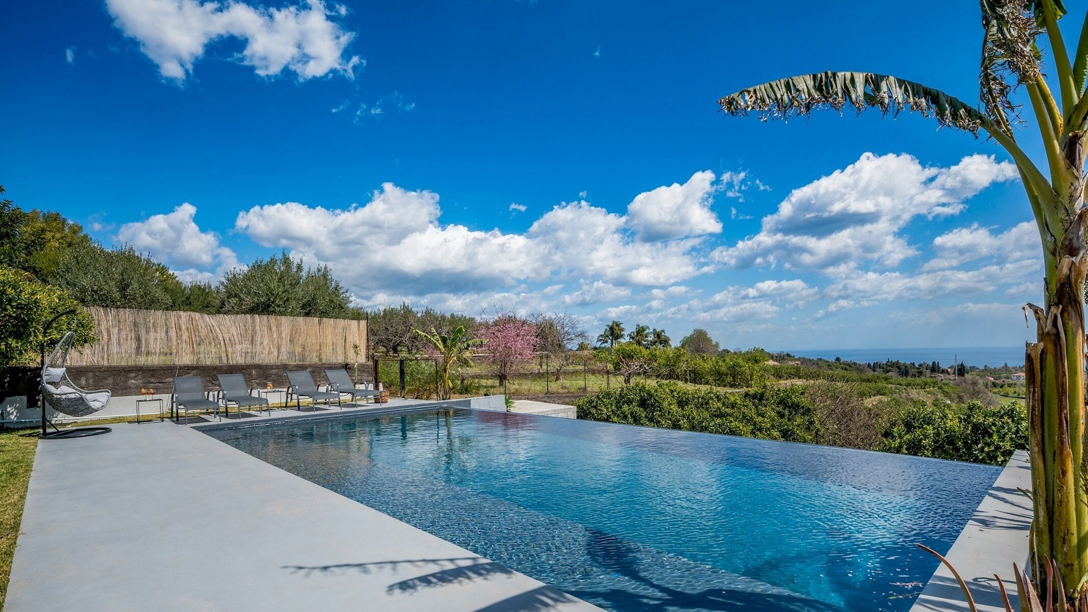 En rektangulär infinitypool med en klarblå himmel och några få moln i bakgrunden.