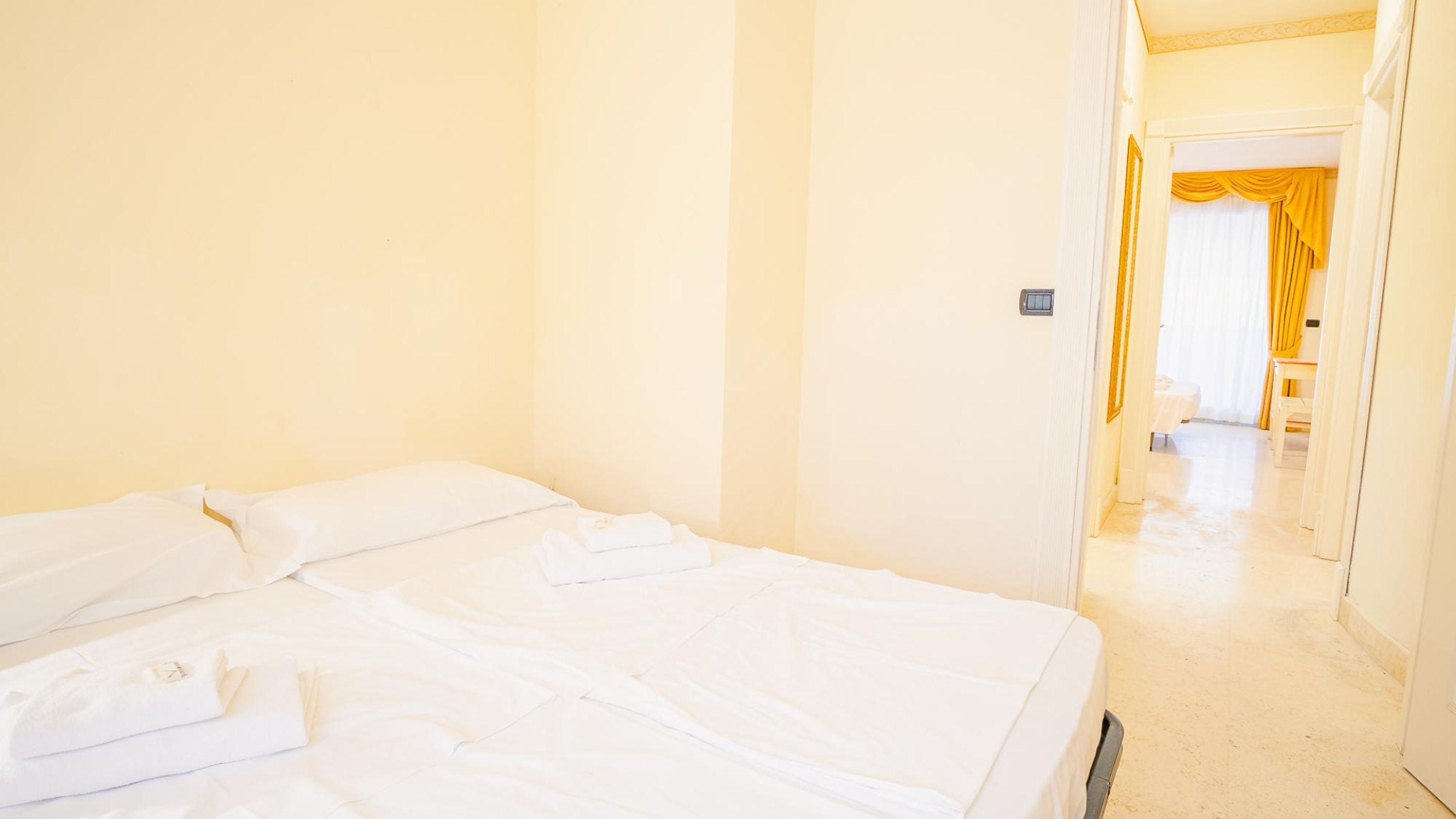 Ein Hotelzimmer mit einem Bett, einer Tür zu einem Flur und einem Fenster mit Vorhängen.