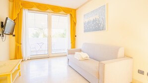 A room with a sofa, a TV mounted on the wall, and a balcony with yellow curtains. - 2 Relais du Lac Village - Italian Homing (Desenzano del Garda)