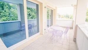 A balcony with a table and chairs, glass doors, and a view of greenery. - 206 Relais du Lac Village - Italian Homing (Desenzano del Garda)
