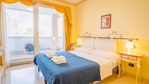 A hotel room with a bed, two bedside tables with lamps, a window with yellow curtains, and a poster on the wall. - 201 Relais du Lac Village - Italian Homing (Desenzano del Garda)