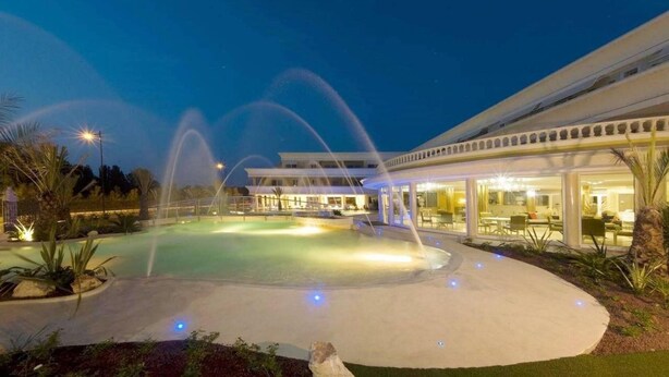 A well-lit outdoor pool area with water features, a covered seating area, and a building with large windows. - 201 Relais du Lac Village - Italian Homing (Desenzano del Garda)