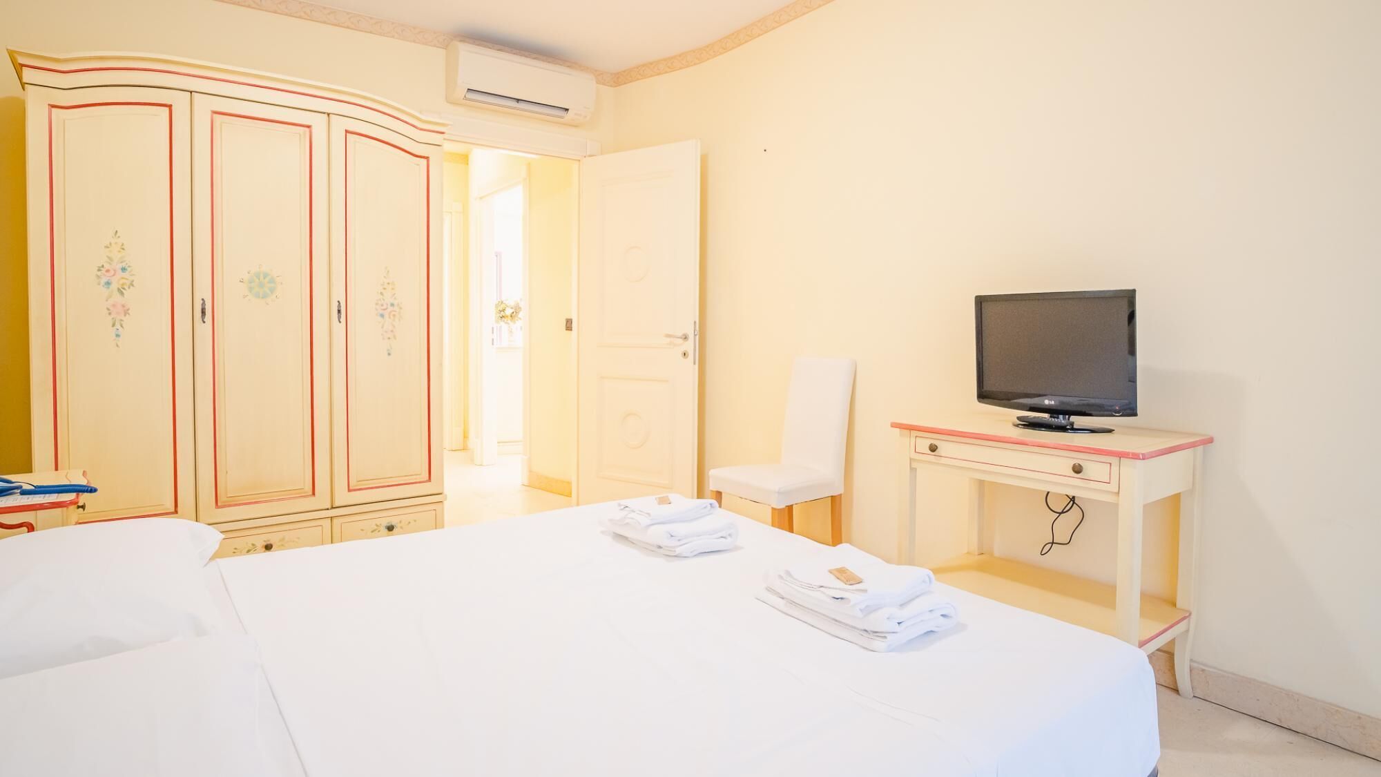 A hotel room with a bed, a TV on a desk, a wardrobe, and a bathroom door.