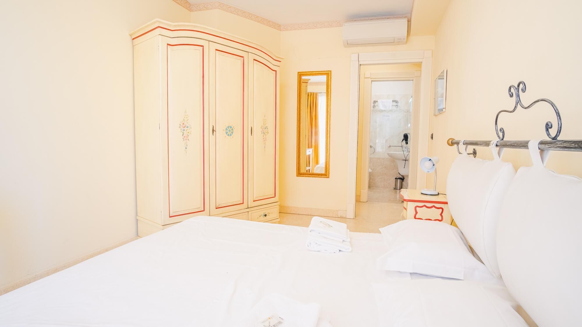 Une chambre d’hôtel avec un lit, une armoire, un miroir et une petite table avec une lampe.