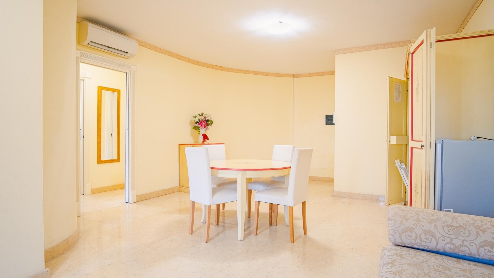 Een kamer met een eettafel en stoelen, een bank en een koelkast.