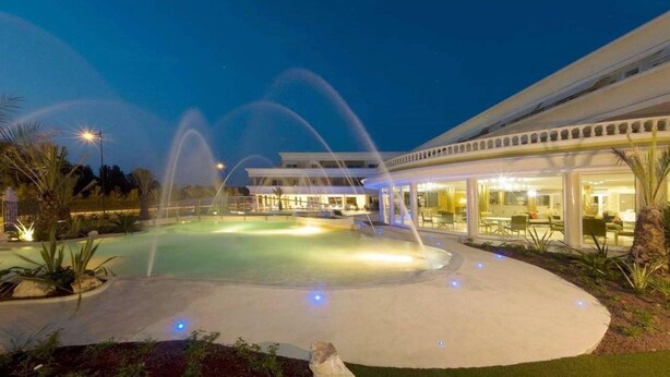 A well-lit outdoor pool area with water features, a covered seating area, and a building with large windows. - 104 Relais du Lac Village - Italian Homing (Desenzano del Garda)