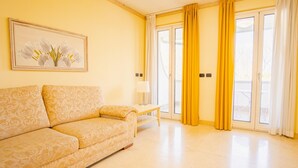 A room with a sofa, a small table, a lamp, and a sliding glass door with yellow curtains. - 104 Relais du Lac Village - Italian Homing (Desenzano del Garda)