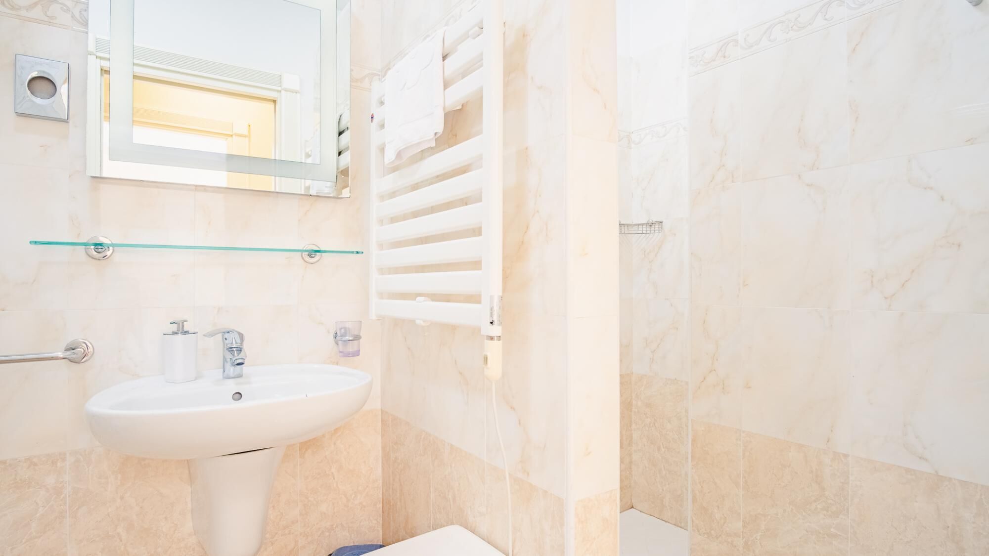 A bathroom with a white sink, a mirror, and a glass shelf.