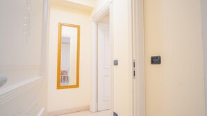 Un pasillo con una puerta blanca, un espejo con marco dorado y un interruptor de luz en la pared.