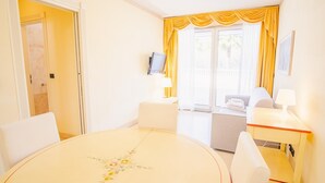 Habitación de hotel con una mesa redonda, dos sillas, un sofá, un televisor y una ventana con cortinas amarillas.