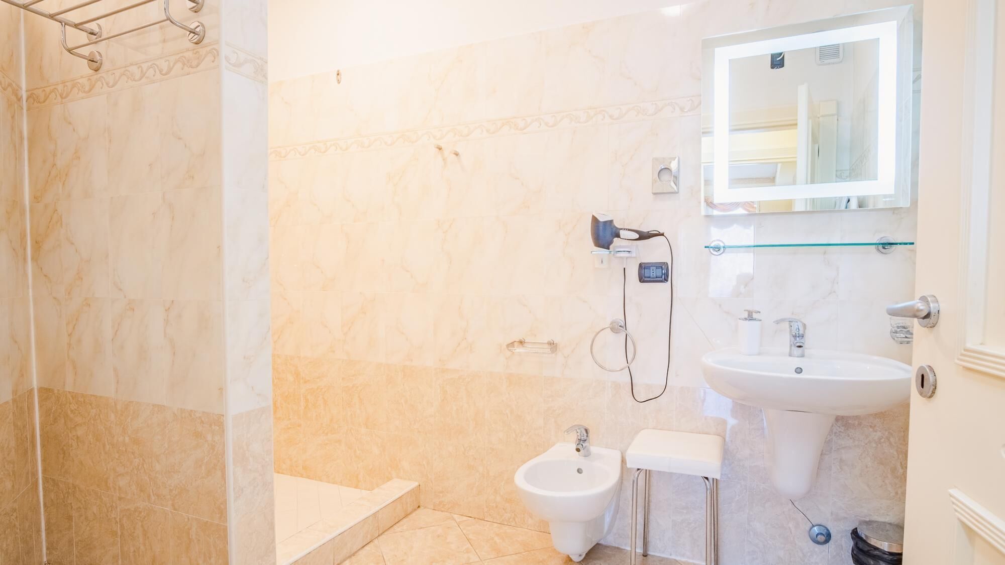 Une salle de bain avec un sol en marbre, un bidet, un lavabo et une douche à parois de verre.