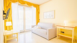 Habitación de hotel con sofá, una mesita de noche con lámpara, escritorio con lámpara y un cuadro en la pared.