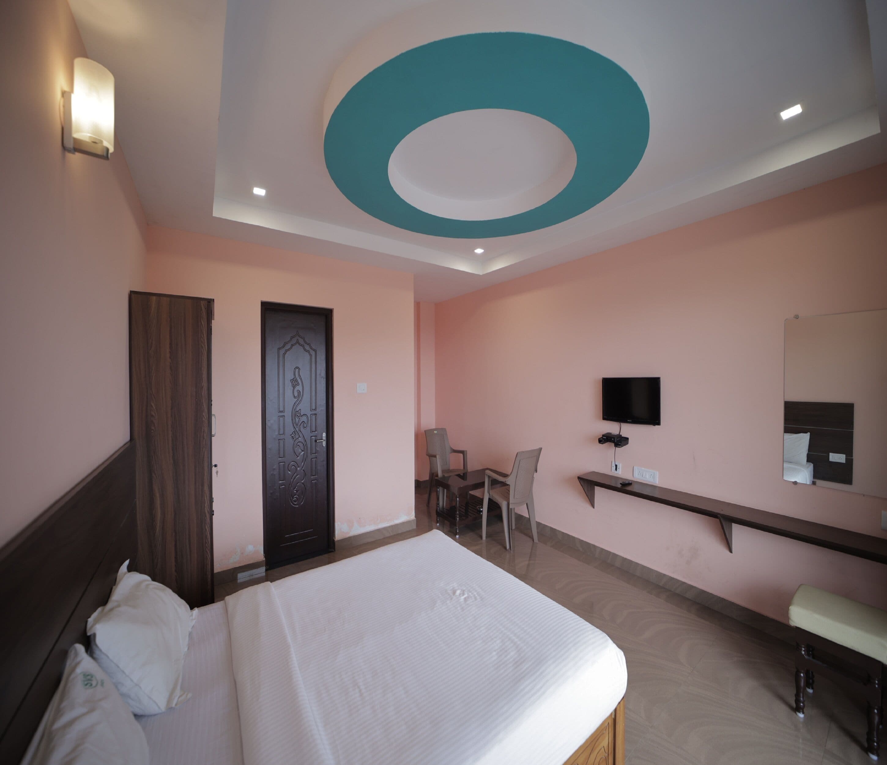 A hotel room with a bed, a desk, a chair, a TV, and a mirror.