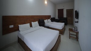 A hotel room with two beds, a wooden headboard, a small wooden table, a TV mounted on the wall, and a door with a curtain. - Cool Stay Home (Kodaikanal)