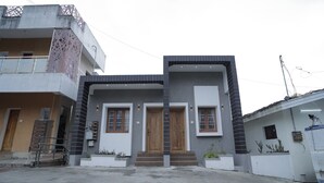 A modern two-story house with a flat roof, two wooden doors, and a balcony with a metal railing. - Cool Stay Home (Kodaikanal)