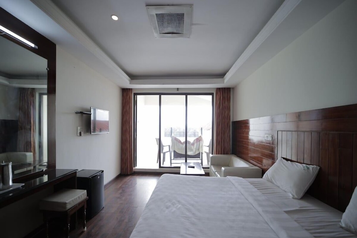 A hotel room with a large bed, a desk with a chair, a television, and a window with curtains.
