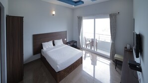 A modern hotel room with a large bed, a flat-screen TV, a balcony with a view, and a ceiling with blue accents. - Cool Stay Home (Kodaikanal)