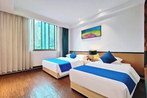 A hotel room with two beds, a large window with curtains, a painting on the wall, and a wooden floor.