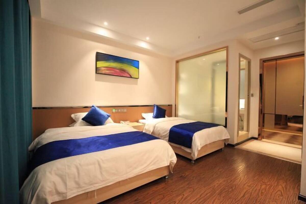 Une chambre d’hôtel avec deux lits, un tableau au mur et une porte coulissante donnant sur une salle de bain.