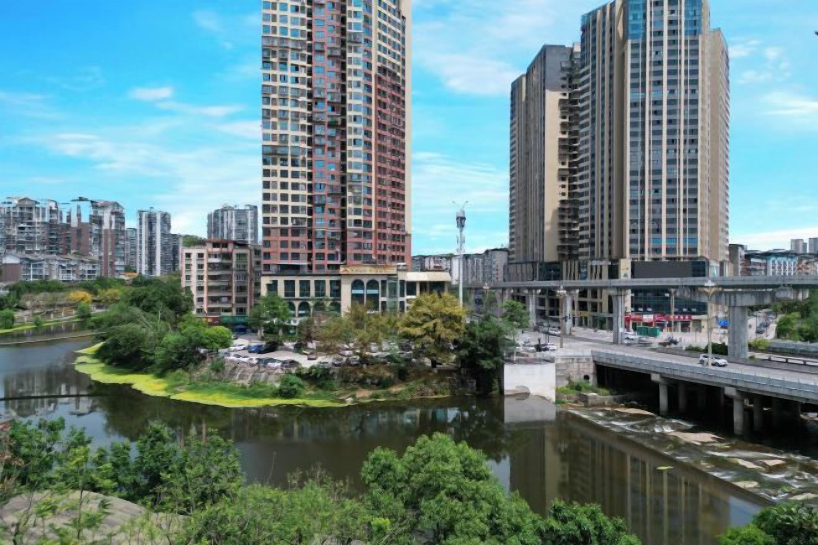 Un río con un puente, rodeado de vegetación y edificios altos.