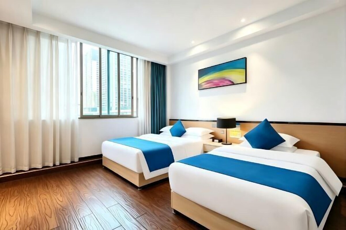 A hotel room with two beds, a large window, and a painting on the wall.