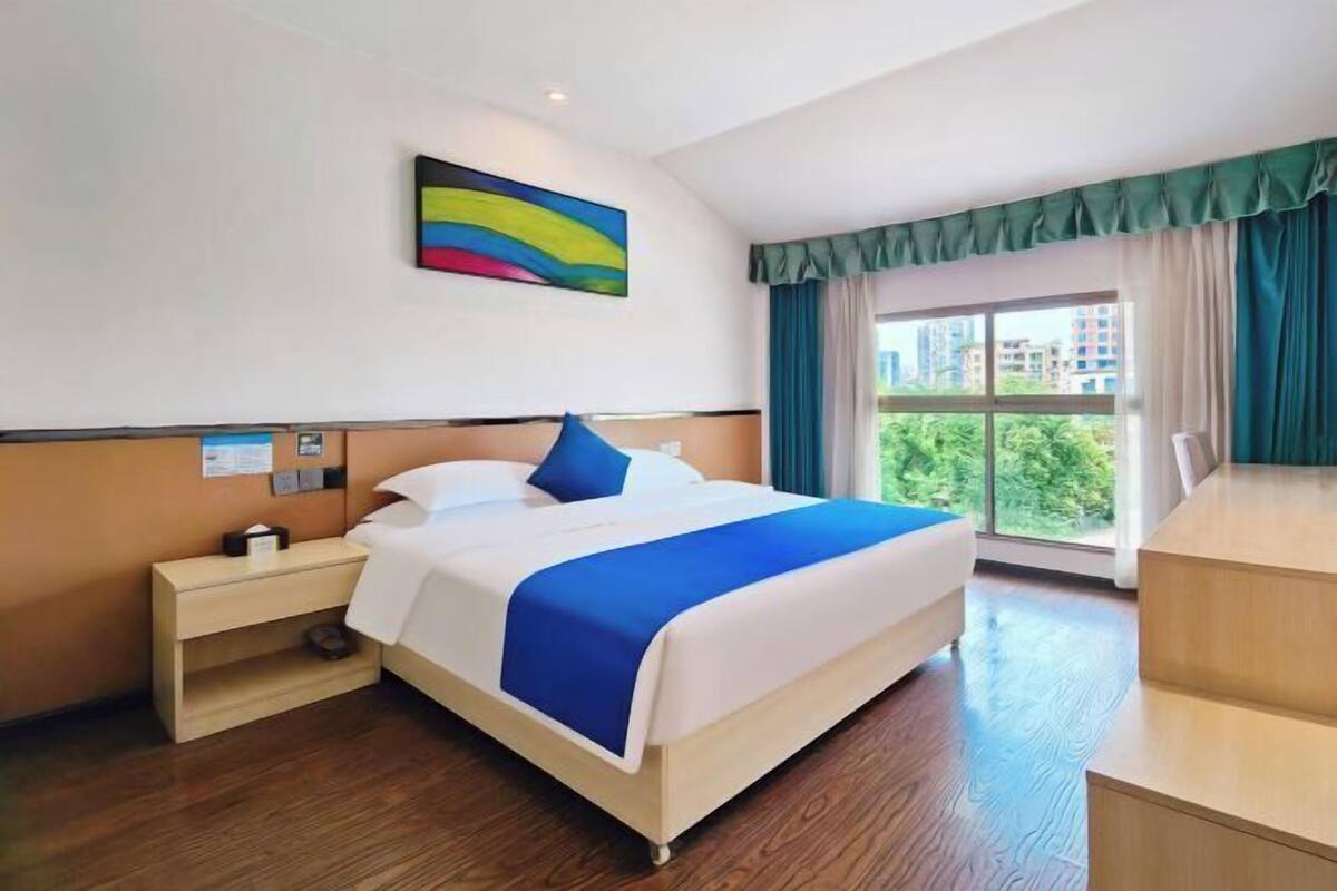 Une chambre d’hôtel avec un grand lit, une table de chevet, un bureau et une fenêtre avec des rideaux.