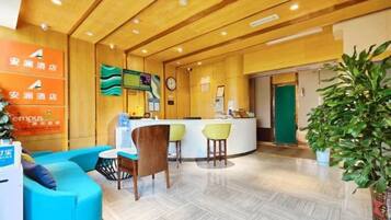 A hotel reception area with a reception desk, seating area, and a large potted plant.