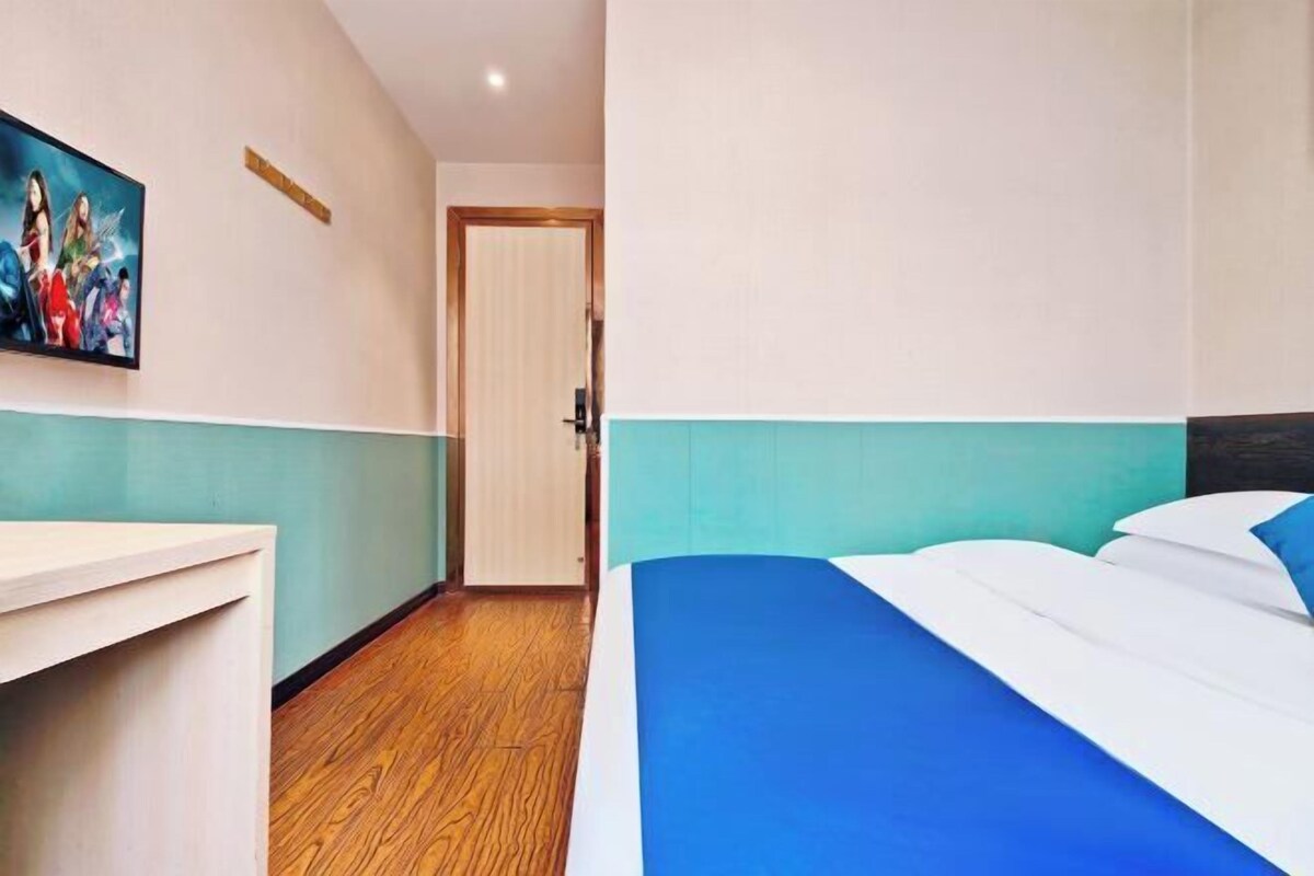 A hotel room with a bed, a desk, and a door.