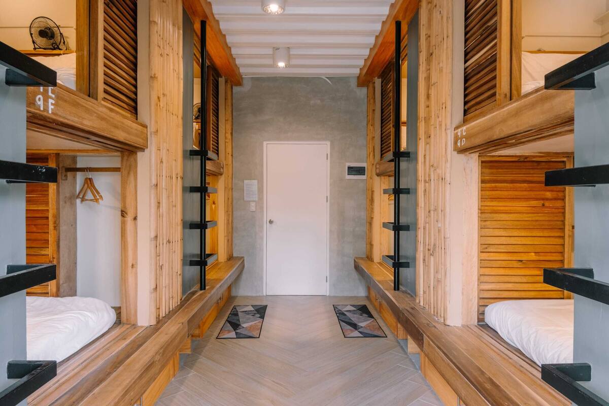 A corridor with bunk beds, wooden beams, and a white door at the end.