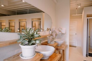 A modern bathroom with a large mirror, white sink, and potted plants.