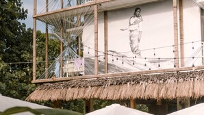 A tropical outdoor seating area with thatched-roof structures, wooden tables, and chairs. - Happiness Hostel Siargao (General Luna)