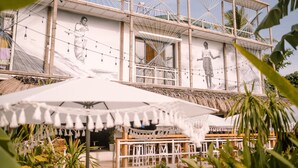 A building with a large mural, outdoor seating, and a thatched roof structure. - Happiness Hostel Siargao (General Luna)
