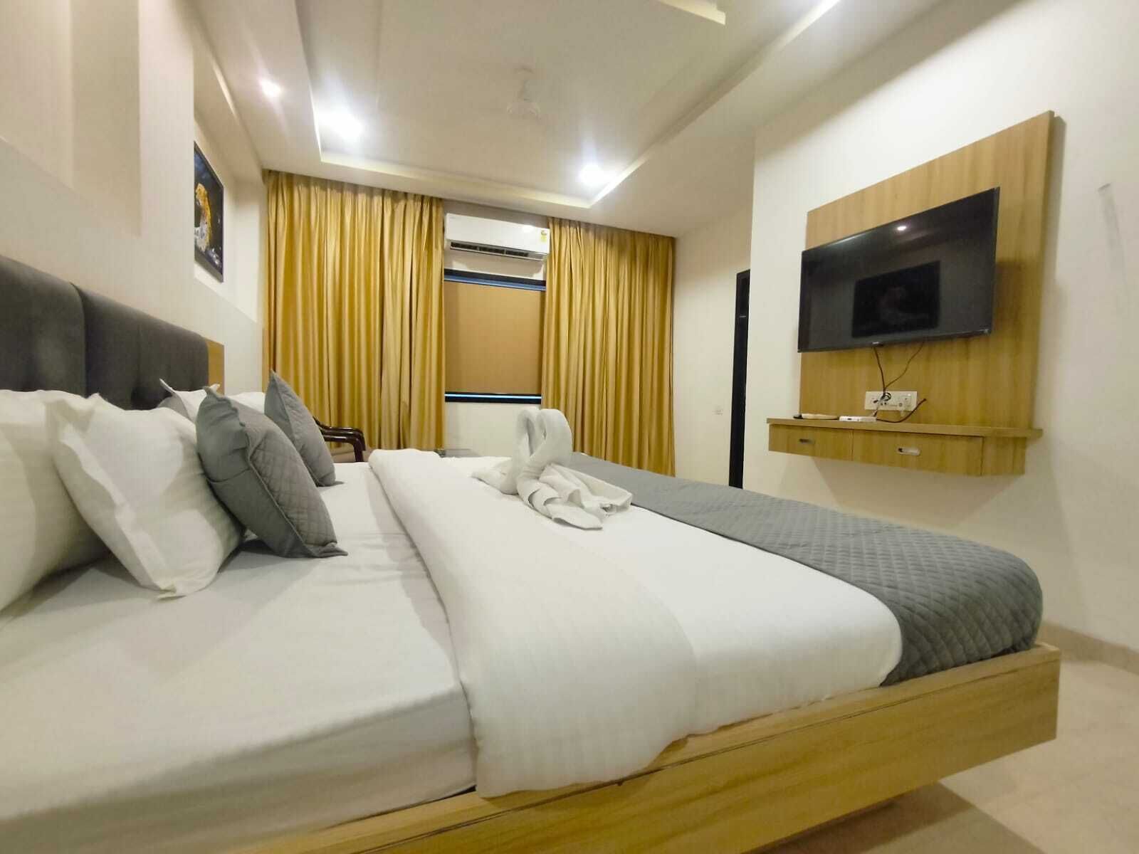 A modern hotel room with a large bed, a flat-screen TV mounted on the wall, and an air conditioning unit.