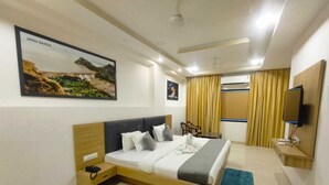 A modern hotel room with a large bed, a desk, a television, and a painting of a landscape.