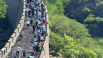 A crowded walkway on a steep, curved stone wall with a watchtower at the top.