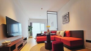 Un salon moderne doté d’un téléviseur à écran plat, d’un canapé d’angle rouge, d’une table basse ronde et d’une grande fenêtre avec des rideaux.