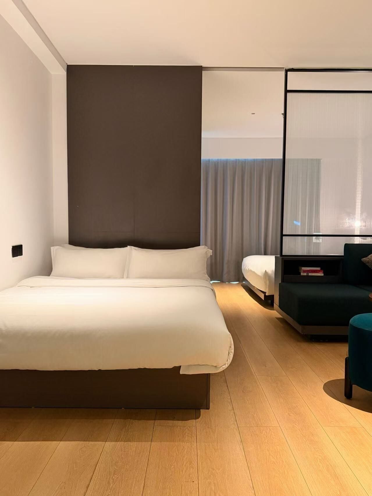 A modern hotel room with a large bed, a seating area, and a large window with curtains.