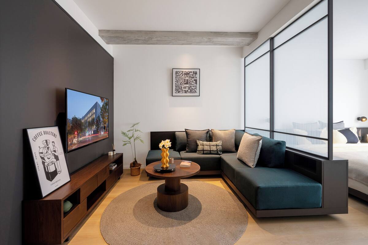 A modern living room with a large TV, a sofa, a coffee table, and a large window.