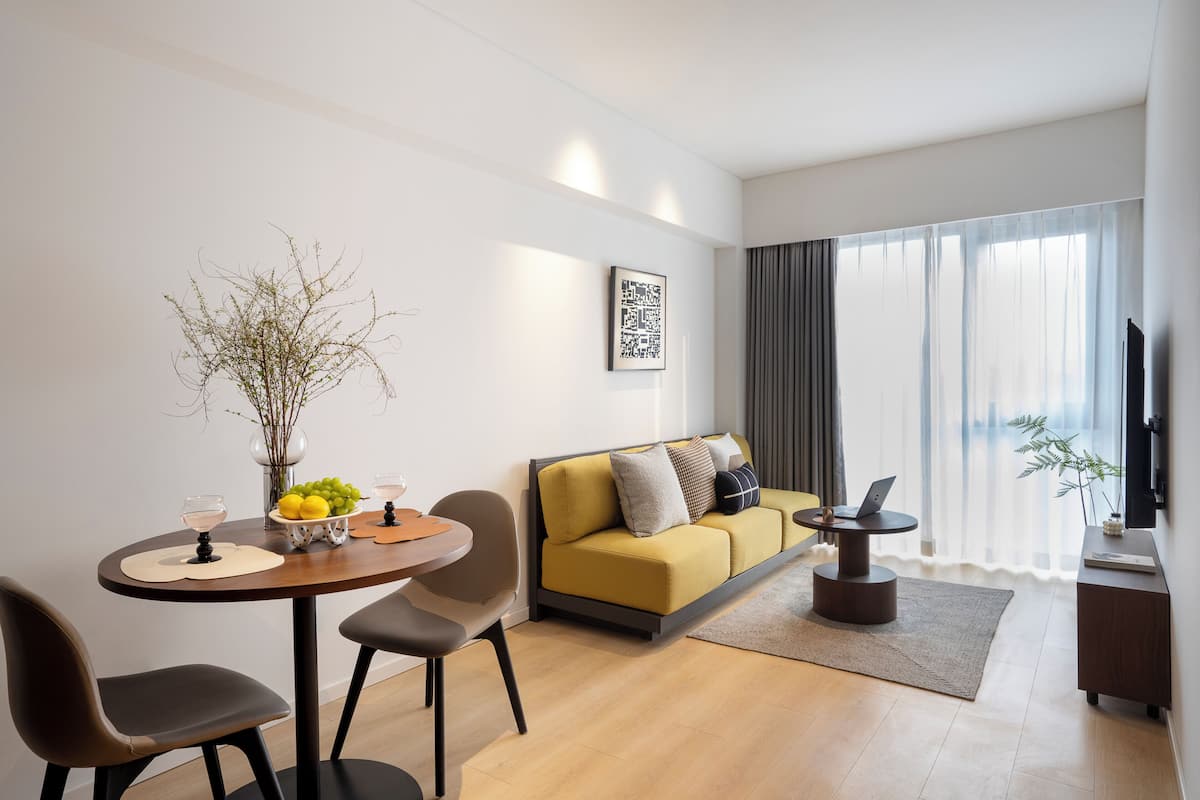 A modern living room with a sofa, a dining table with chairs, a small coffee table, and a TV on a stand.