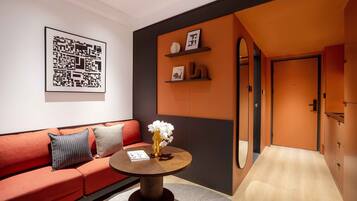 A modern hotel room with a red sofa, a round wooden coffee table with a vase of flowers, and a framed abstract artwork on the wall.